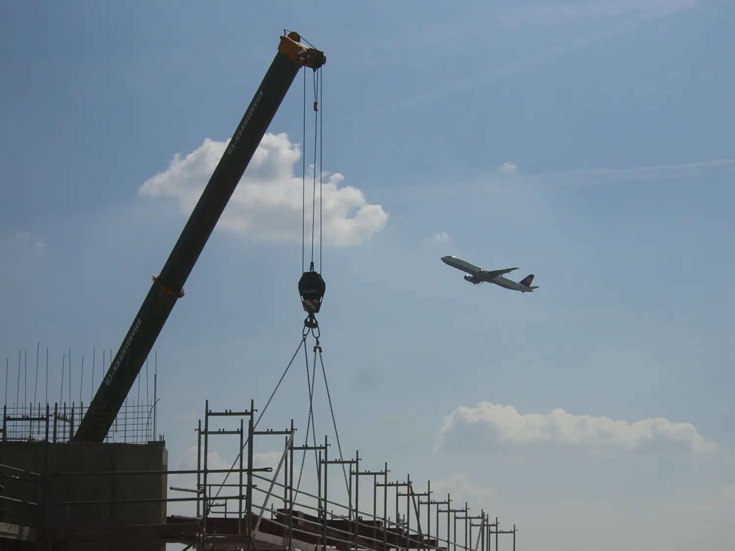 Morana Engineering UG, Kran hebt Gewicht und das Flugzeug fliegt hoch im Hintergrund